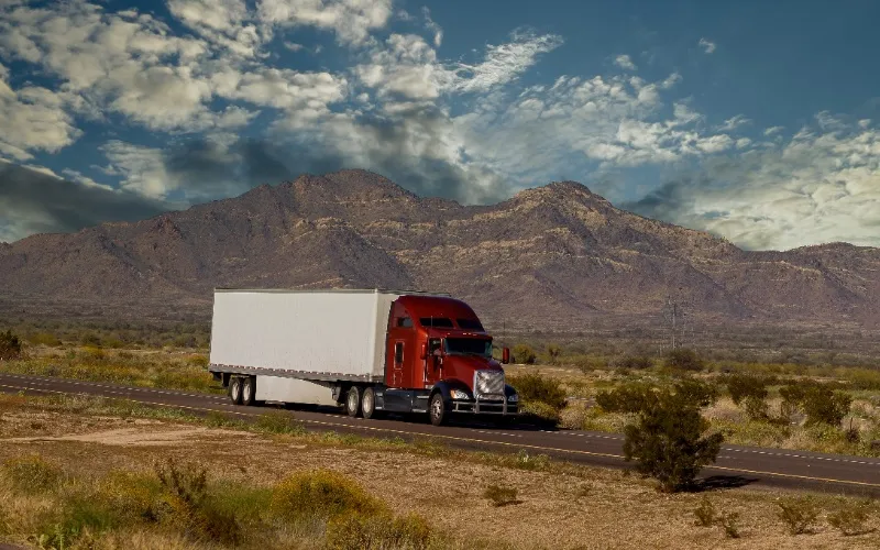 Semi truck hauling dry freight on open highway through desert landscape Semi truck hauling dry freight on open highway through desert landscape